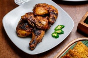 pexels-photo-37179941-37179941 Authentic Indonesian grilled chicken served with fresh green chilies on a traditional plate.